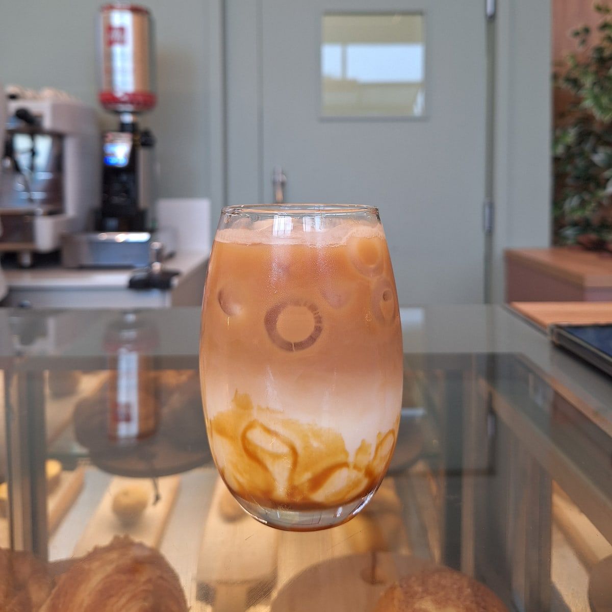 Café gelado em camadas com calda de caramelo no balcão, com a máquina de espresso ao fundo