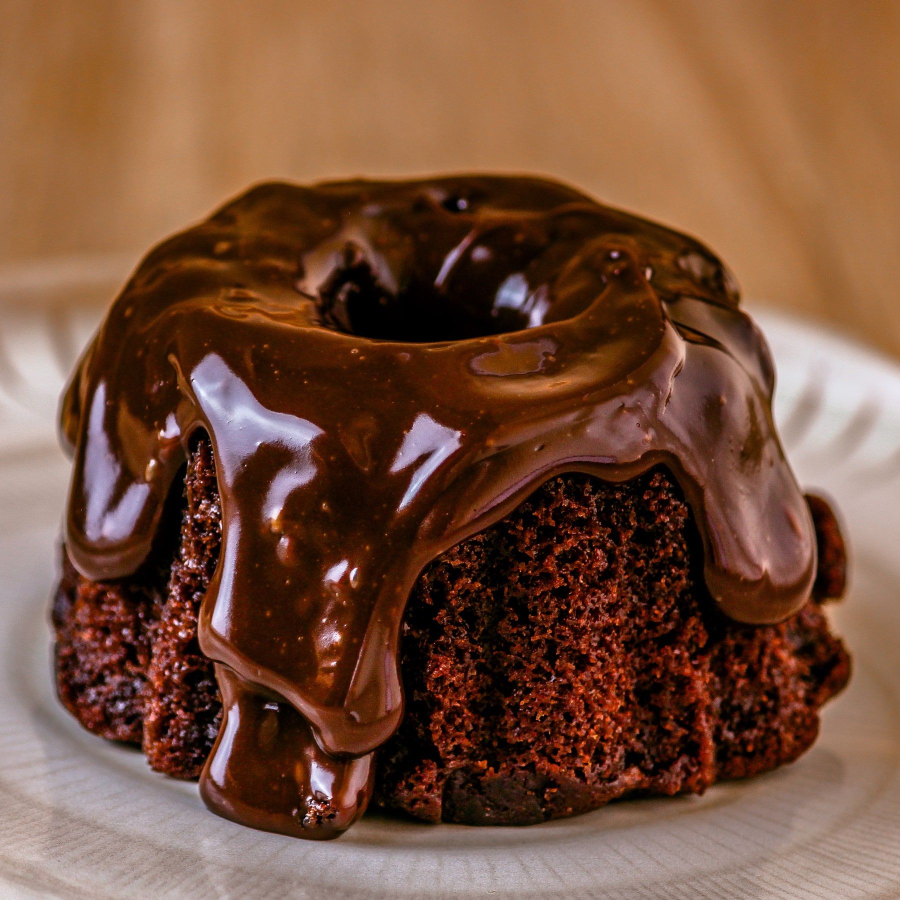 Mini bolo de chocolate com calda de chocolate escorrendo pelos lados, num prato branco