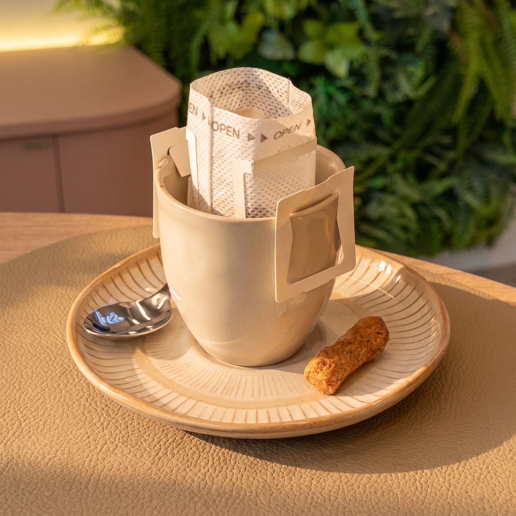 Drip coffee na xícara com o filtro individual de papel, num pires de cerâmica com colherzinha e biscoito, sobre a mesa do salão