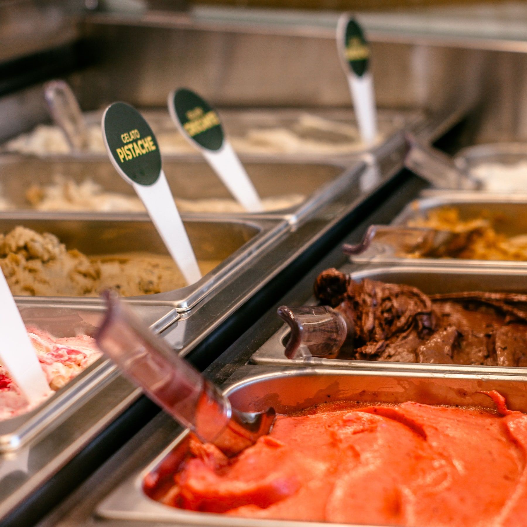 Vitrine de gelato com os sabores em cubas de inox e uma plaquinha com o nome de cada um