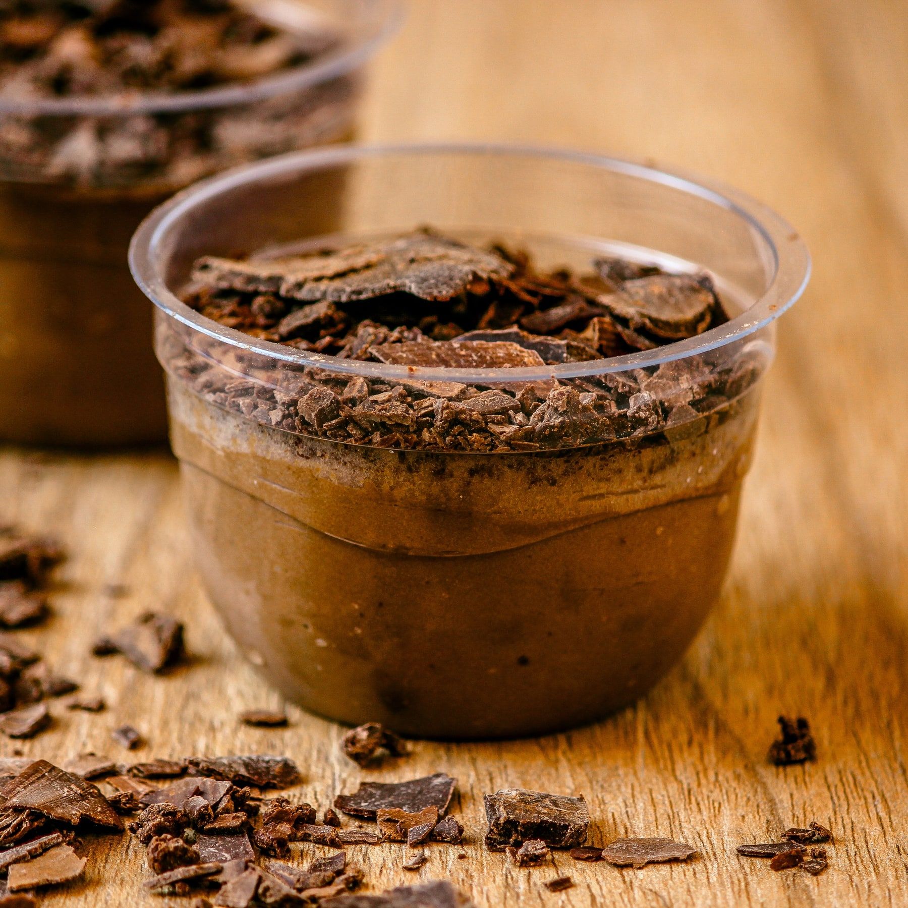 Mousse de chocolate num copinho transparente, com raspas de chocolate em cima e na mesa de madeira