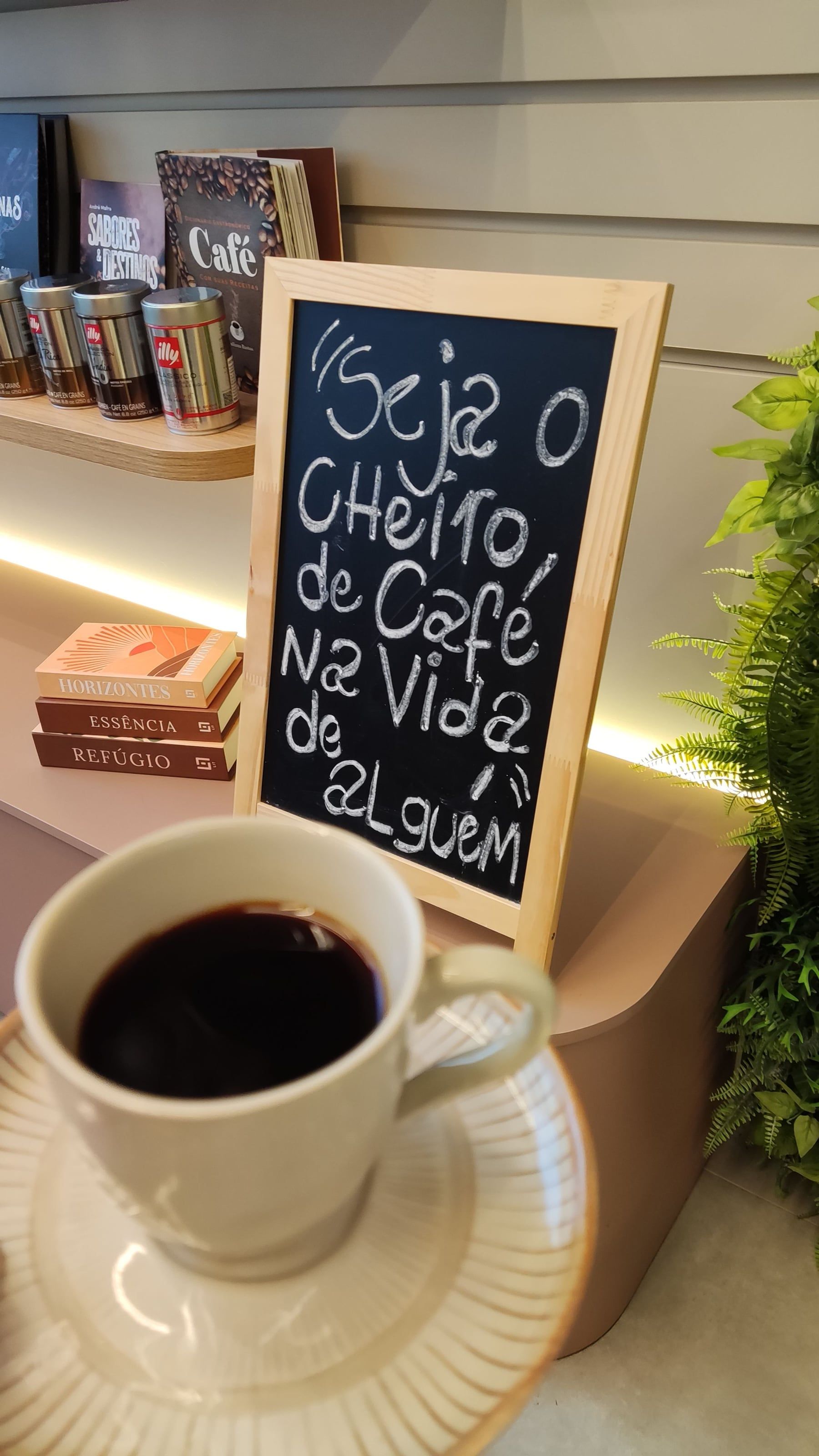 Xícara de café preto diante de uma lousa escrita à mão: Seja o cheiro de café na vida de alguém