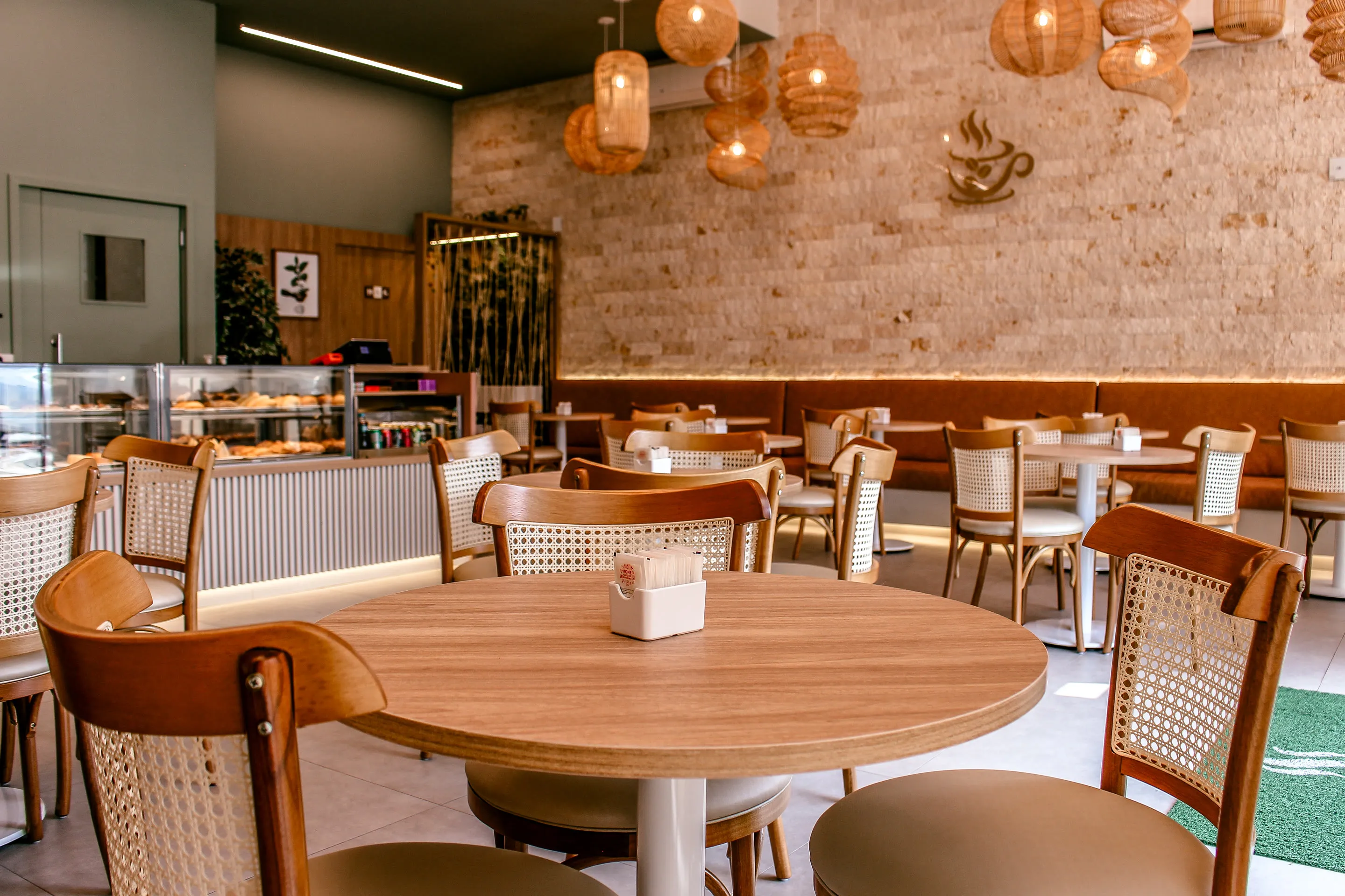 Salão do Café Harmonia com mesas redondas de madeira, cadeiras de palhinha e luminárias de fibra